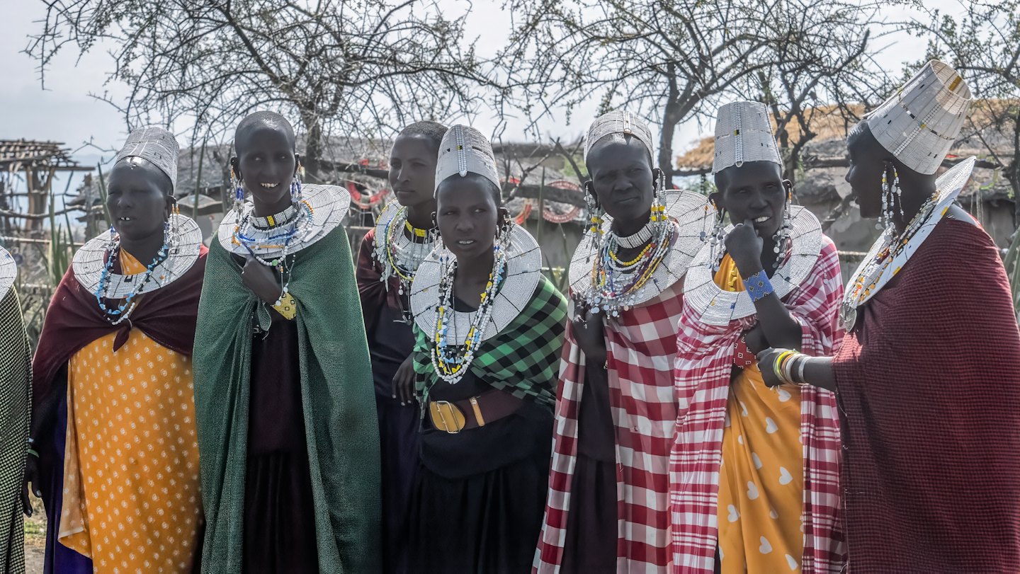Women in traditional beaded jewelry standing together near village huts.